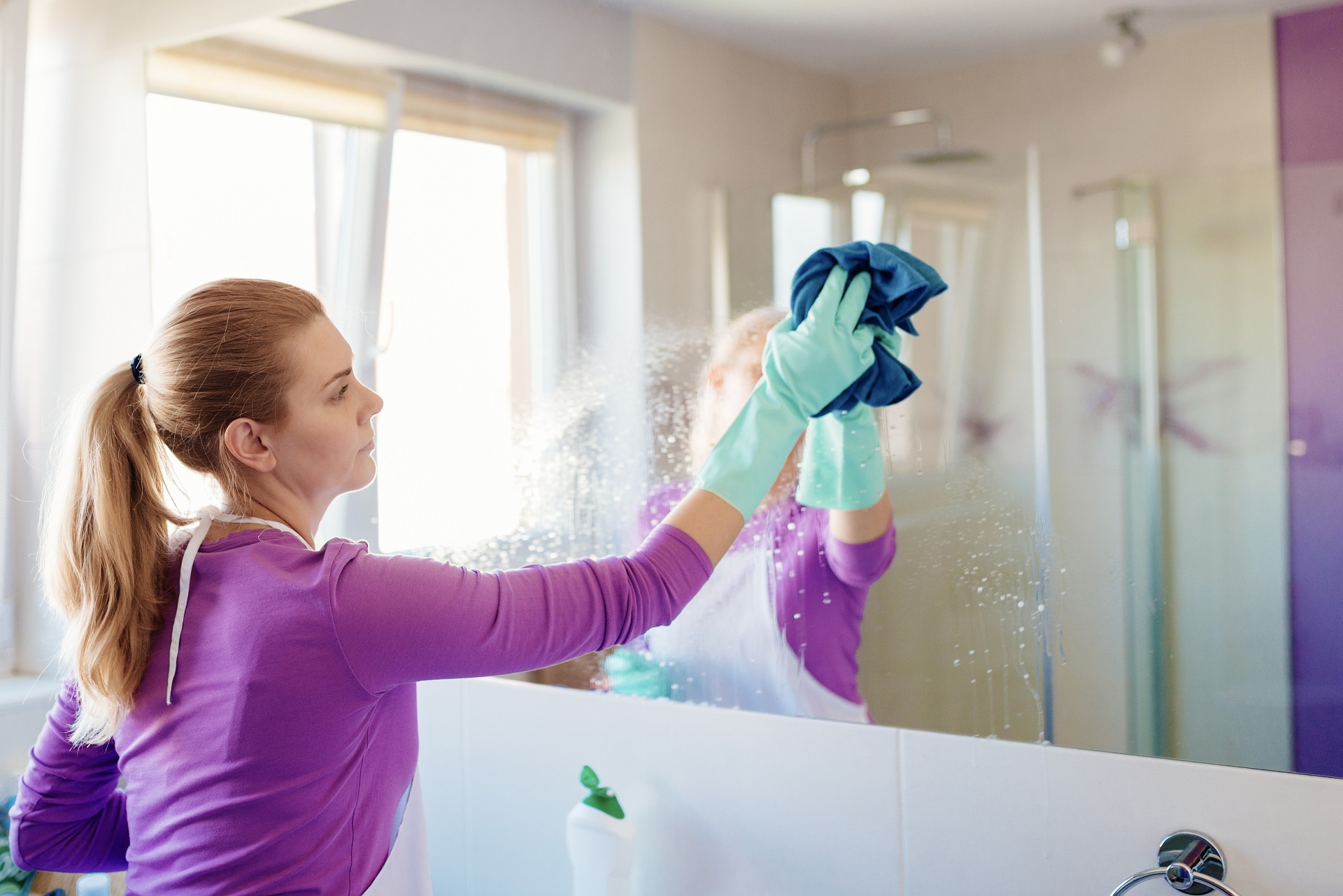 Young beautiful woman in cleaning mirror in bathroom