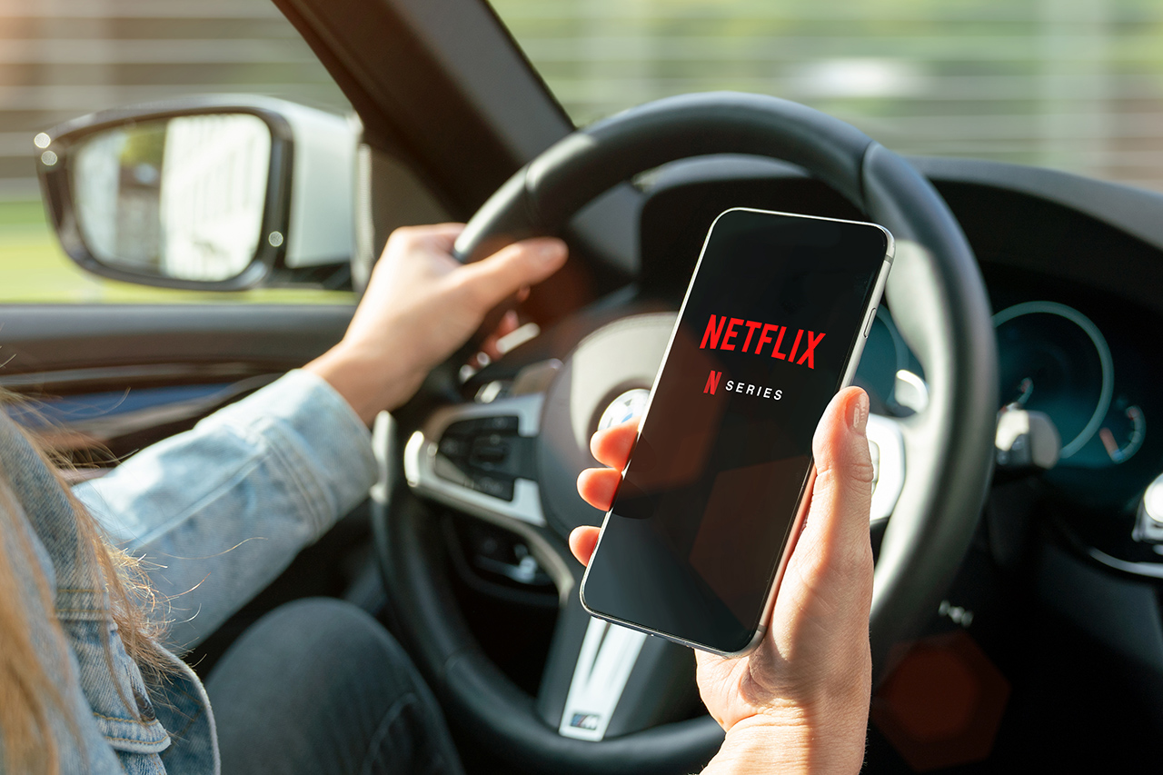 AACHEN, GERMANY – 31. August 2019 : Netflix app on Apple iPhone in car. Young man is browsing the movie video library what to watch.